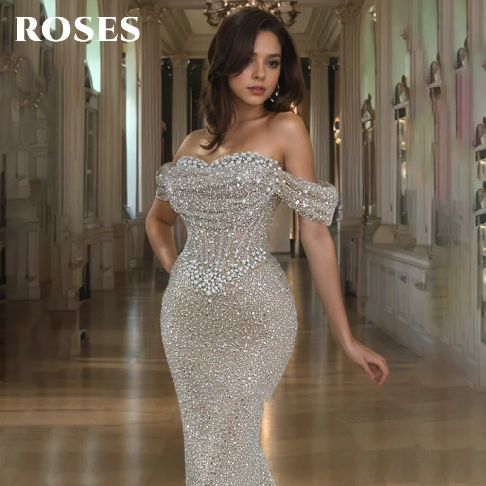 Woman in a sparkling silver off-shoulder gown in an elegant interior setting with 'ROSES' branding.