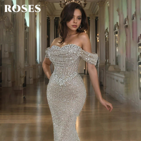 Woman in a sparkling silver off-shoulder gown in an elegant interior setting with 'ROSES' branding.