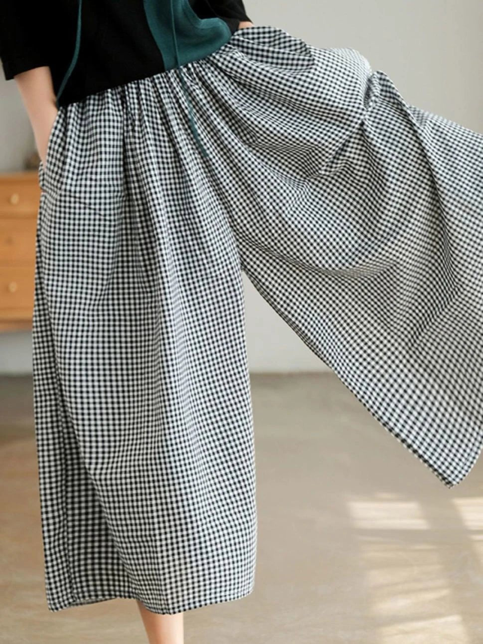 Person wearing a black and white checkered pant in a room with wooden furniture.