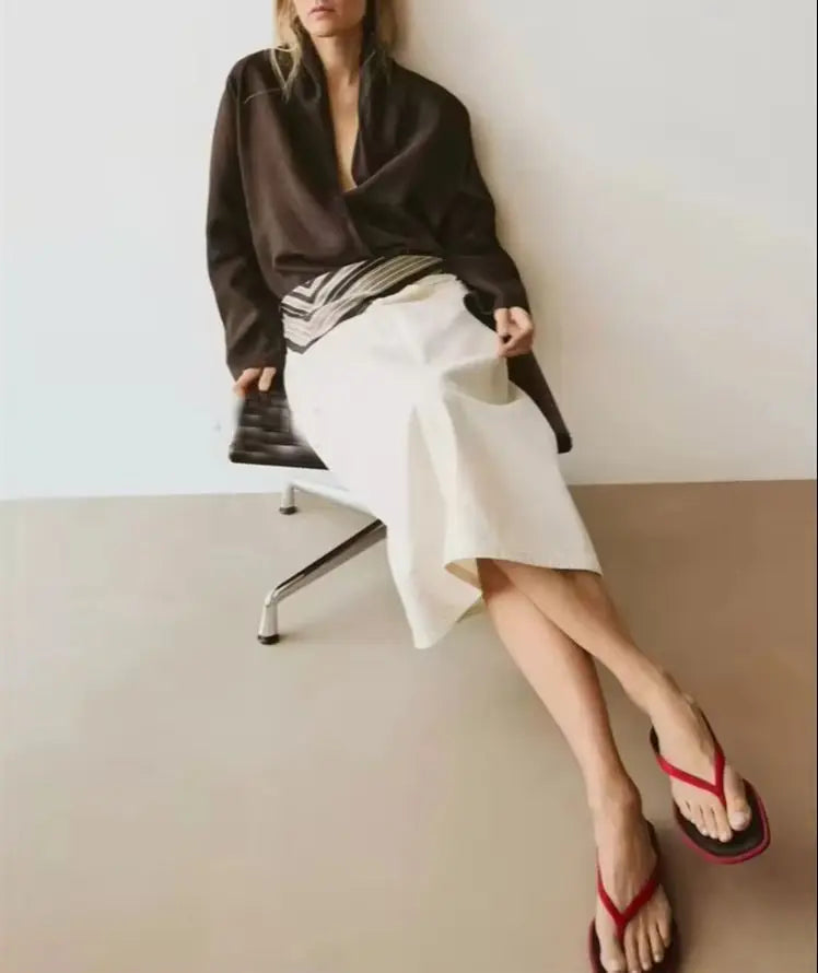 Woman sitting on a chair wearing a black top, white skirt, and red sandals.