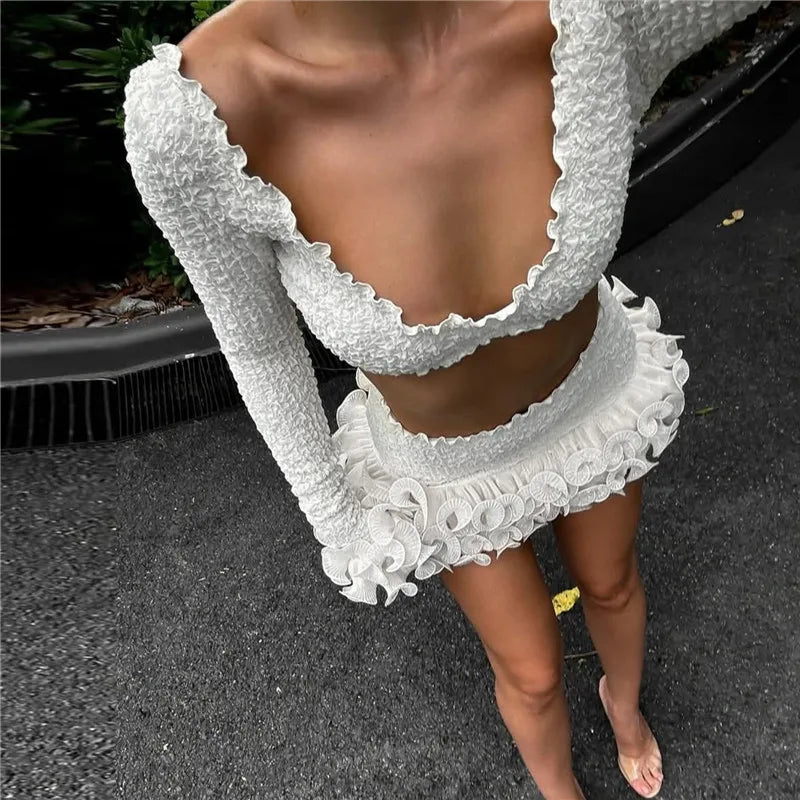White lace dress with long sleeves and ruffled details on a dark surface