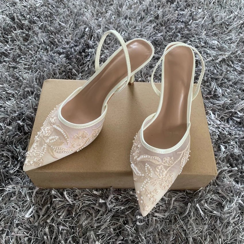 Pair of beige lace high heels on a gold box with a gray textured background