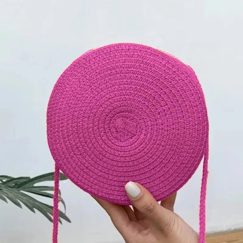 Pink round woven bag held by a hand with a light gray background