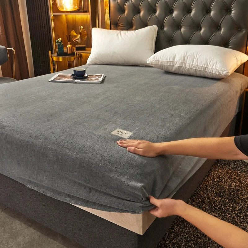 Person adjusting a gray fitted sheet on a bed in a bedroom setting.