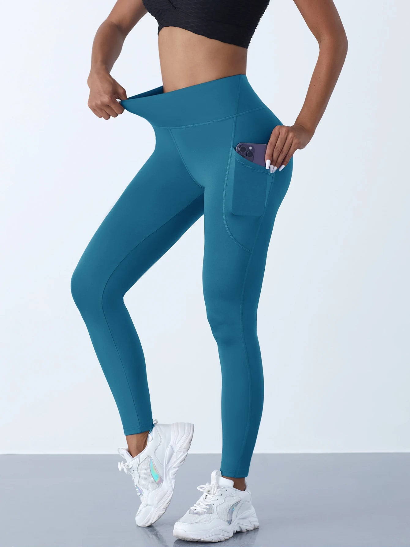 Person wearing teal leggings with a pocket on a light gray background