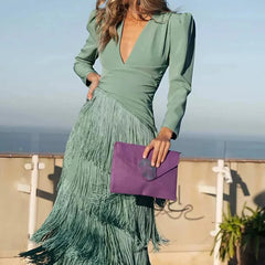 Woman in a green dress with fringe holding a purple clutch against a blurred outdoor background
