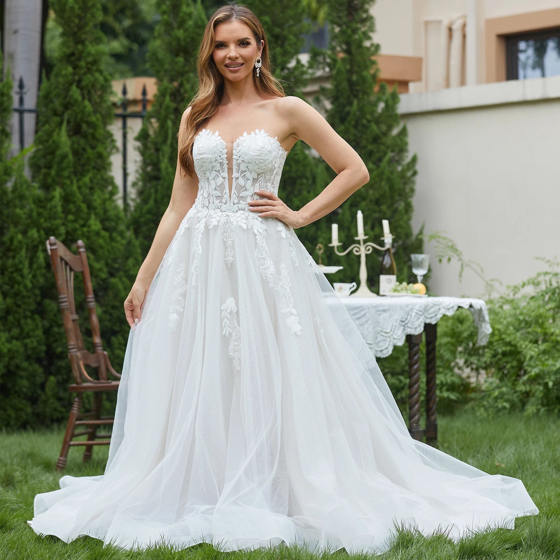 Woman in a white wedding dress standing outdoors with a garden and table in the background