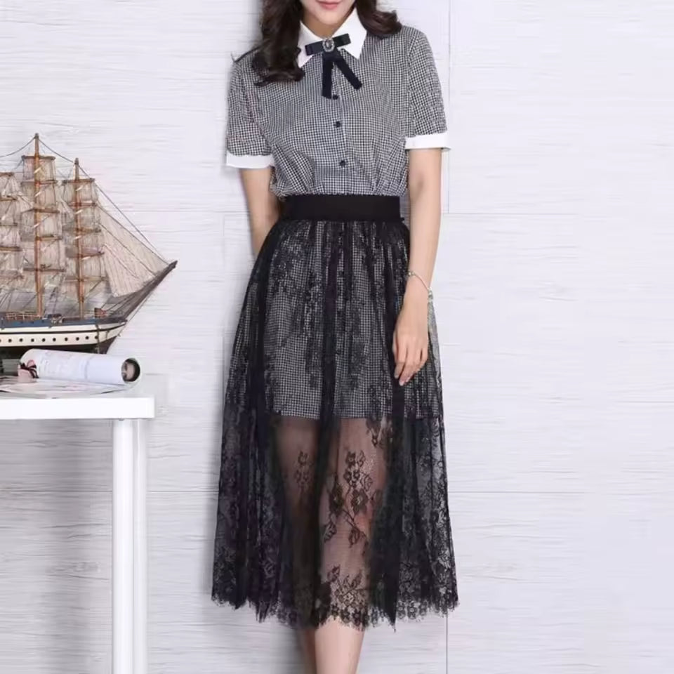 Woman wearing a black and white checkered shirt with a bow tie and a black lace skirt against a white brick wall.