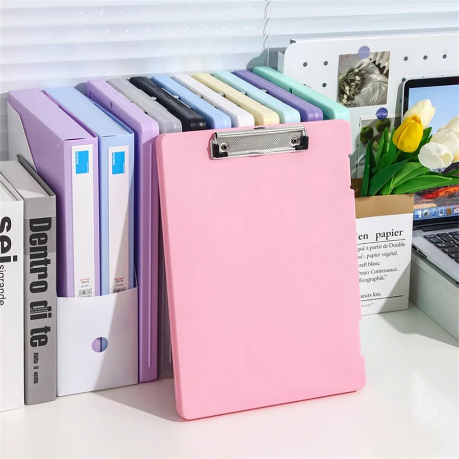 Pink clipboard on a desk with office supplies and a laptop in the background