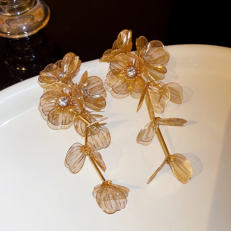 Gold floral earrings on a white surface with a dark background