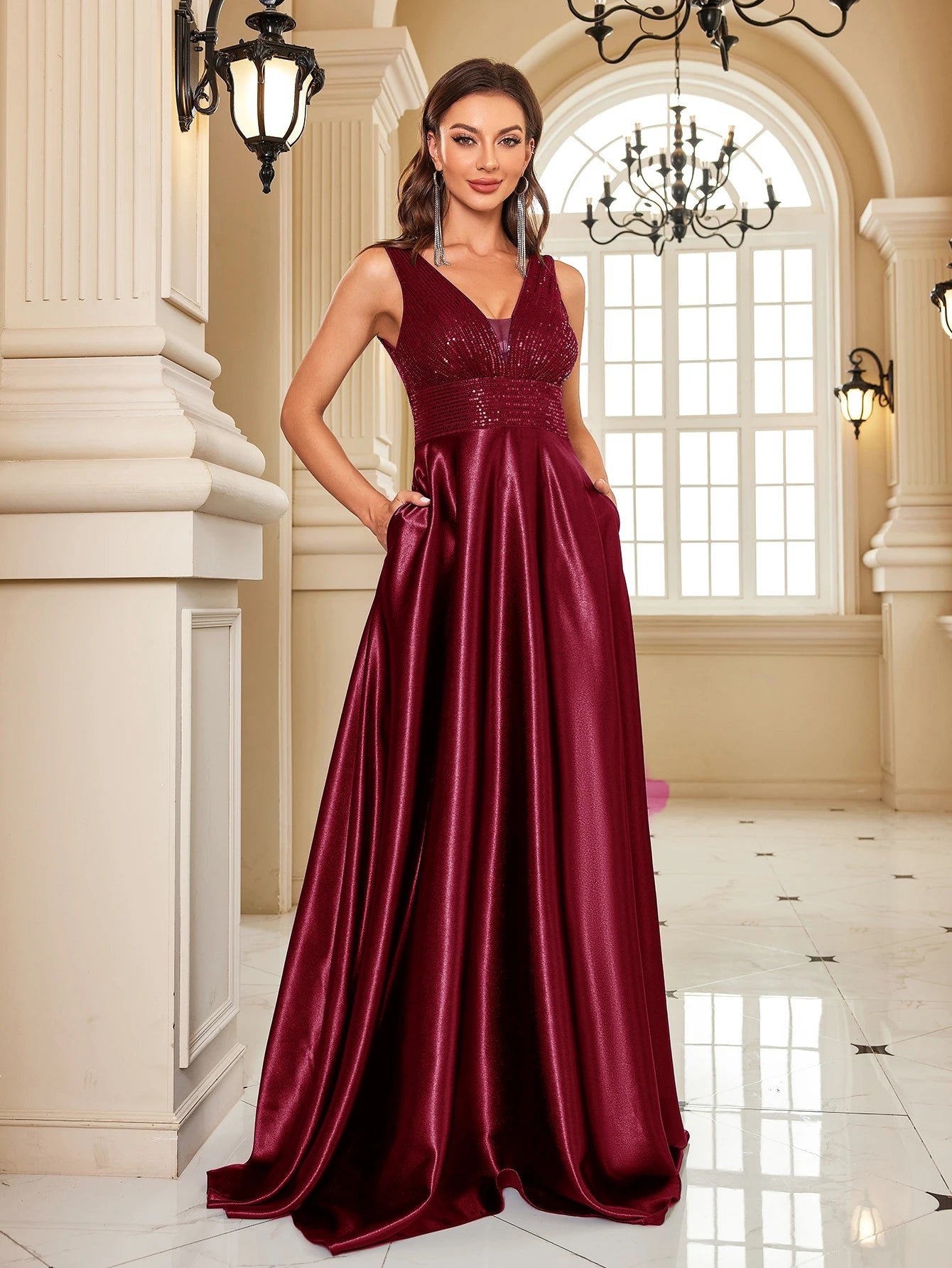 Woman in a burgundy evening gown standing in an elegant interior setting.