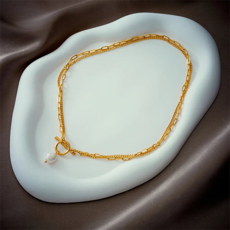 Gold necklace with a pearl pendant on a white dish against a brown fabric background