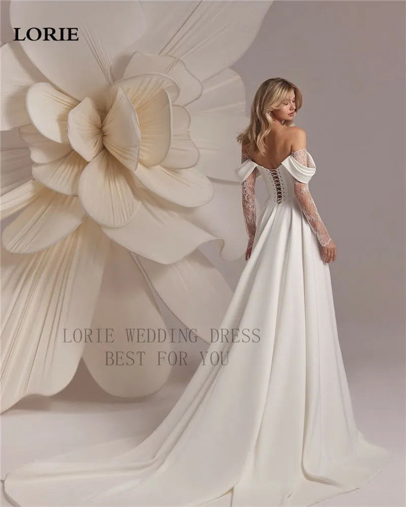 Woman in a white wedding dress standing next to a large floral sculpture with 'LORIE' branding.