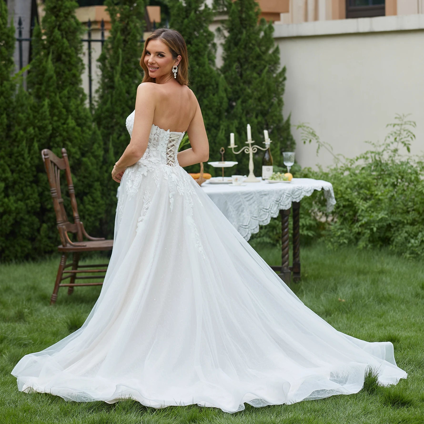 Woman in a white wedding dress standing outdoors with a table and chairs in the background.
