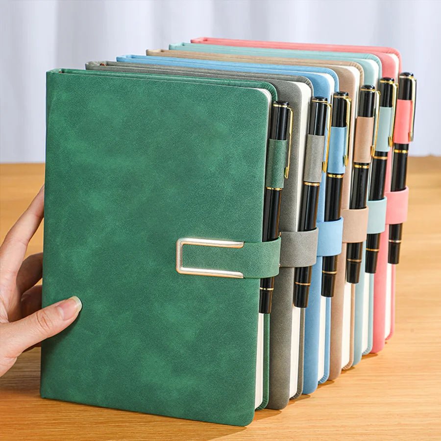 Green notebook held by a hand with other notebooks of different colors arranged on a wooden surface.
