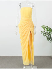Yellow draped dress on a mannequin with a white background and green plant.
