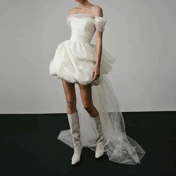 White off-shoulder dress with a tulle skirt and matching knee-high boots on a plain background