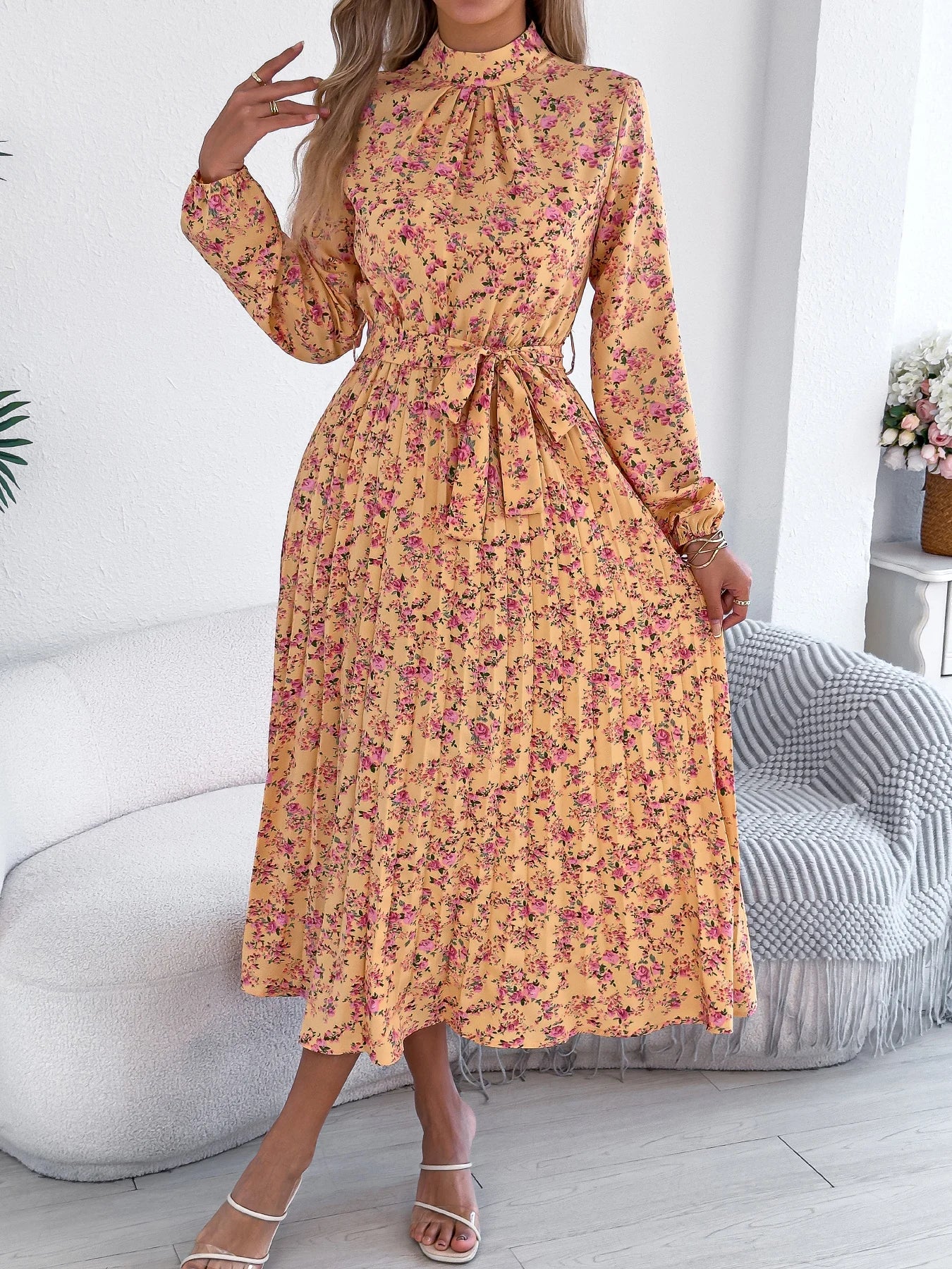 Woman wearing a yellow floral dress in a room with a white wall and gray chair.