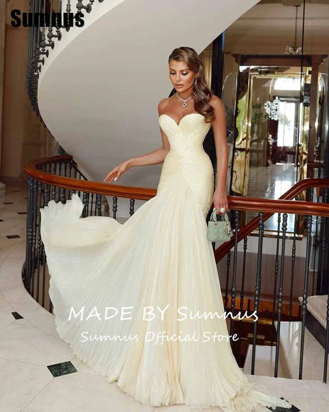 Woman in a white evening gown standing in a luxurious interior setting with 'Sumnus' branding.