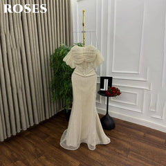 Beige evening gown on a mannequin against a white wall with 'ROSES' branding.