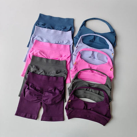Stack of colorful athletic wear including leggings, sports bras, and shorts on a gray background