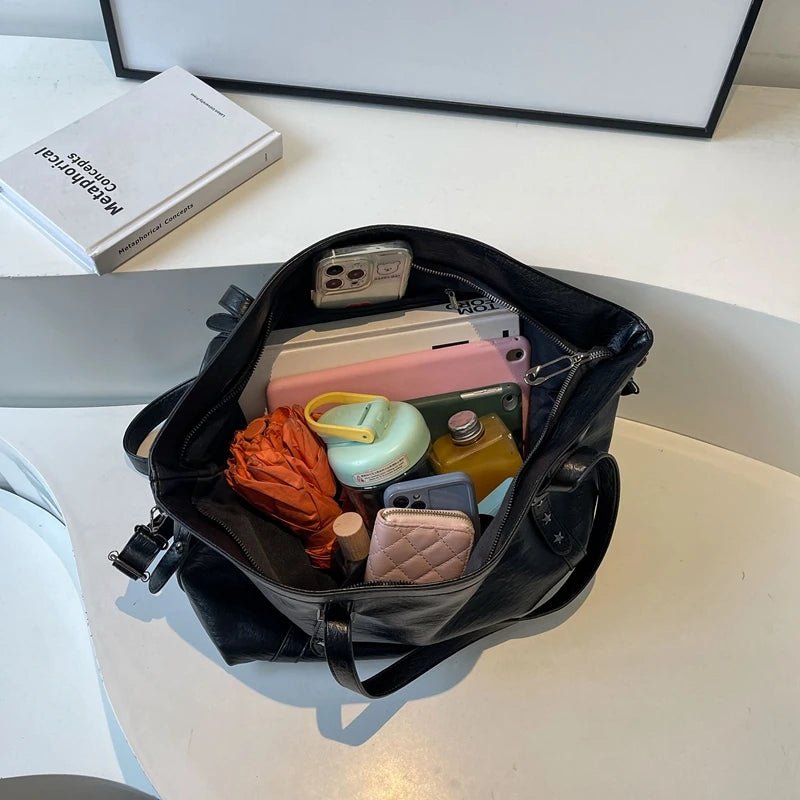 Open black handbag with various items on a light surface