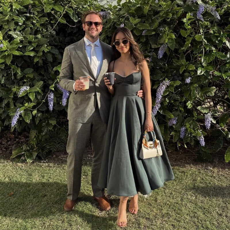 Man and woman in formal attire standing outdoors with greenery in the background