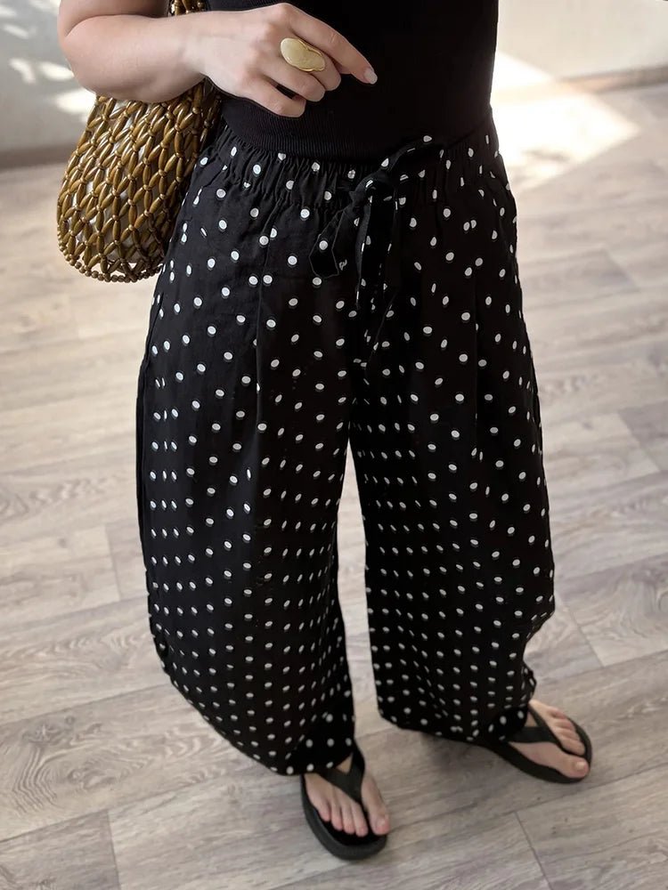 Person wearing black pants with white polka dots on a wooden floor.