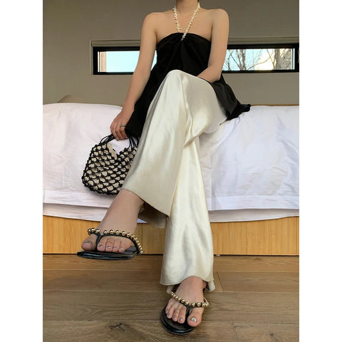 Person wearing a black top and white pants sitting on a bed.