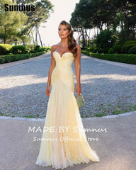 Woman in a yellow evening gown standing on a path with trees and greenery in the background.