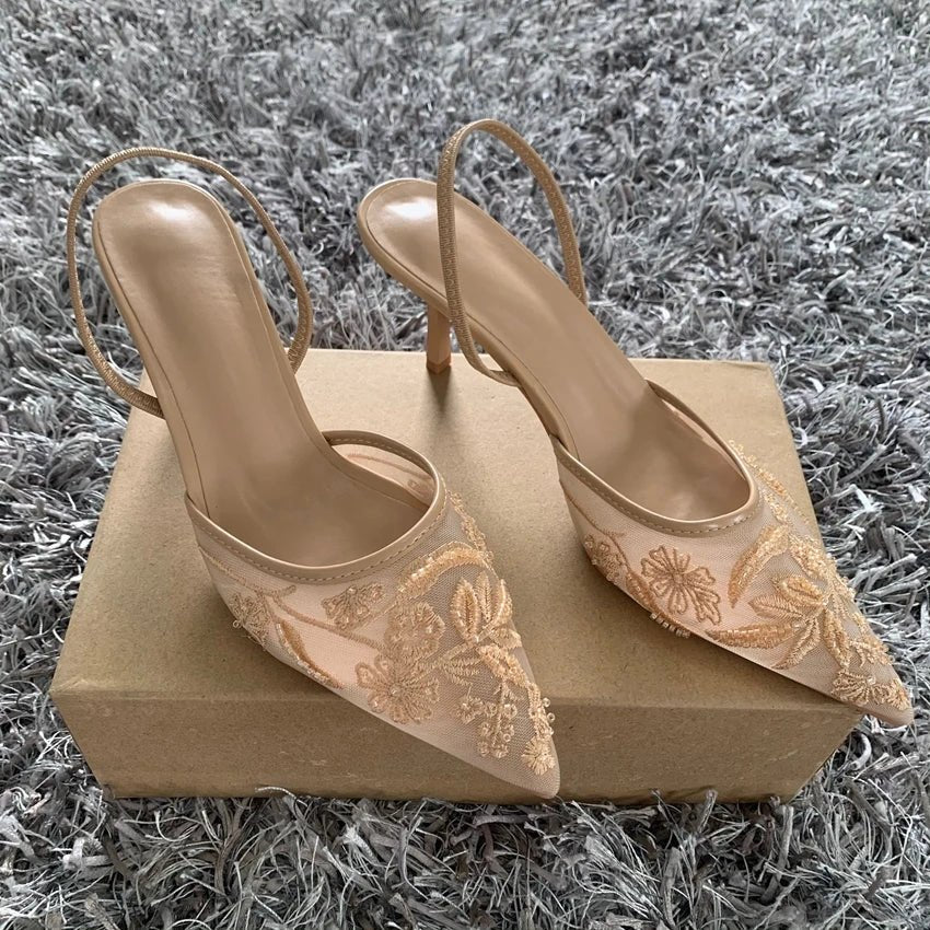 Beige high-heeled shoes with floral embroidery on a beige box against a gray textured background