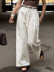 Person wearing white wide-leg pants and a brown top on a street.