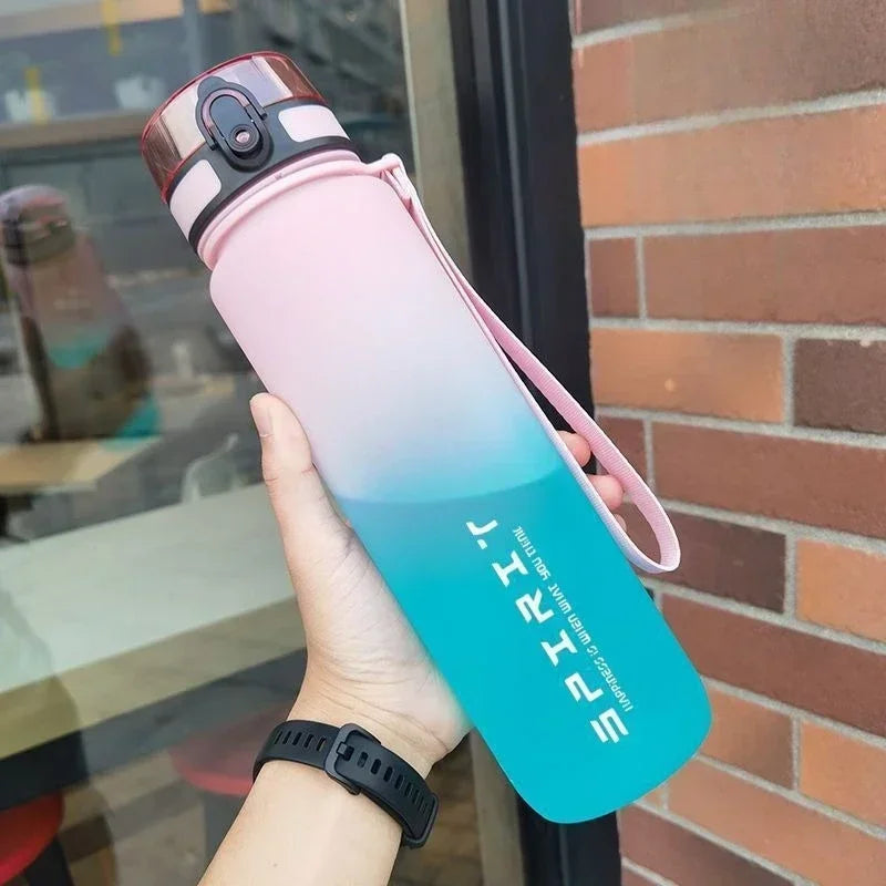Gradient water bottle with pink and blue design held by a person, against a brick wall.