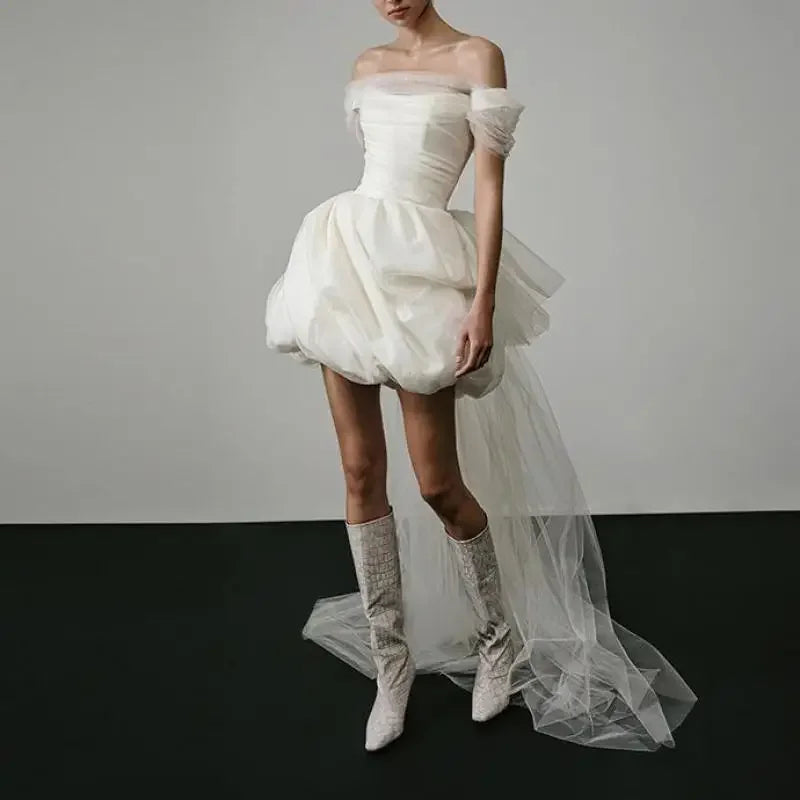 White off-shoulder dress with a tulle skirt worn by a model on a plain background