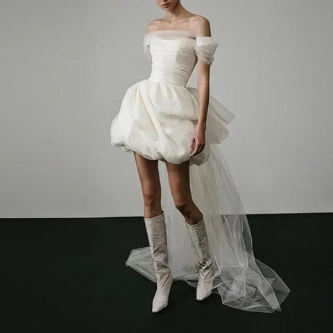 White off-shoulder dress with a tulle skirt worn by a model on a plain background