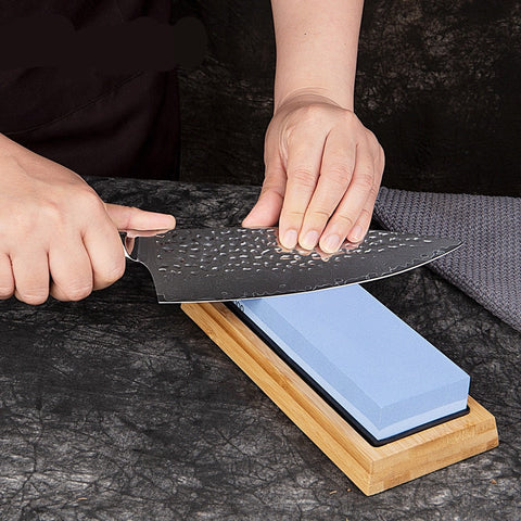 A person sharpening a knife on a blue and white sharpening stone with a black edge.
